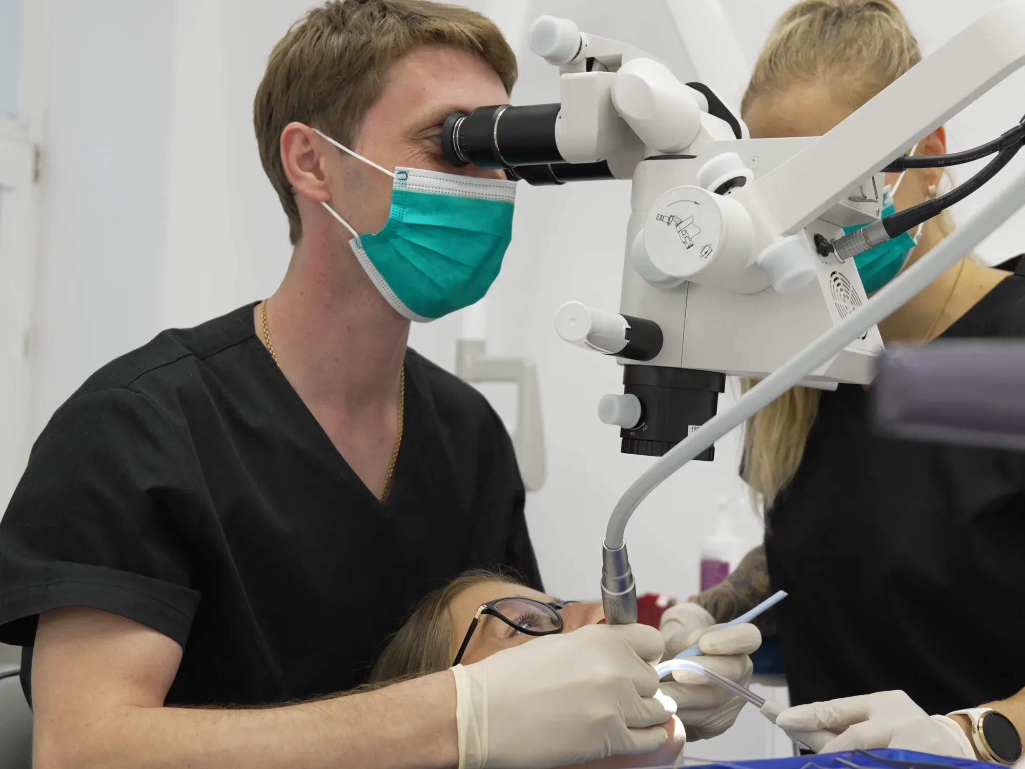 Lékař kliniky STOMADENT ošetřuje kořenové kanálky pod operačním mikroskopem, sestra mu asistuje
